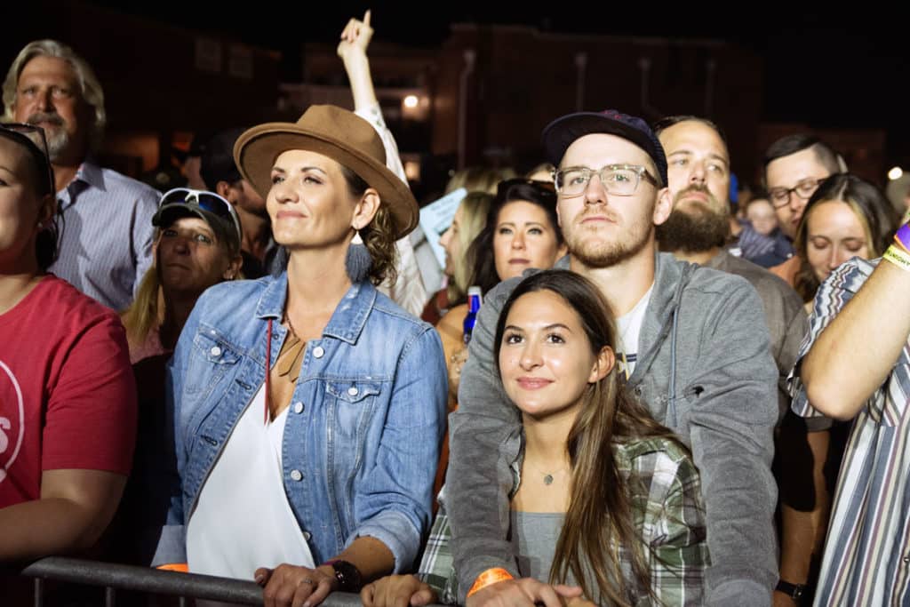 A couple stands and smiles in a crowd of fans enjoying the show at night.