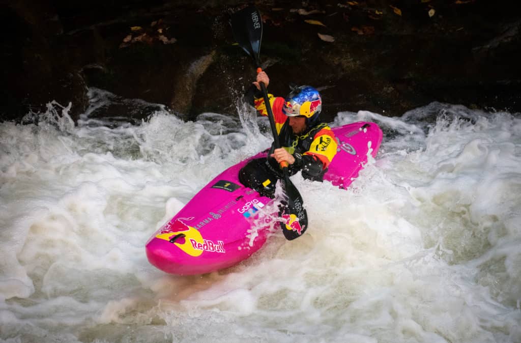 Dane Jackson paddles big foamy white water in a bright pink kayak while wearing gear with RedBull and GoPro logos on it.
