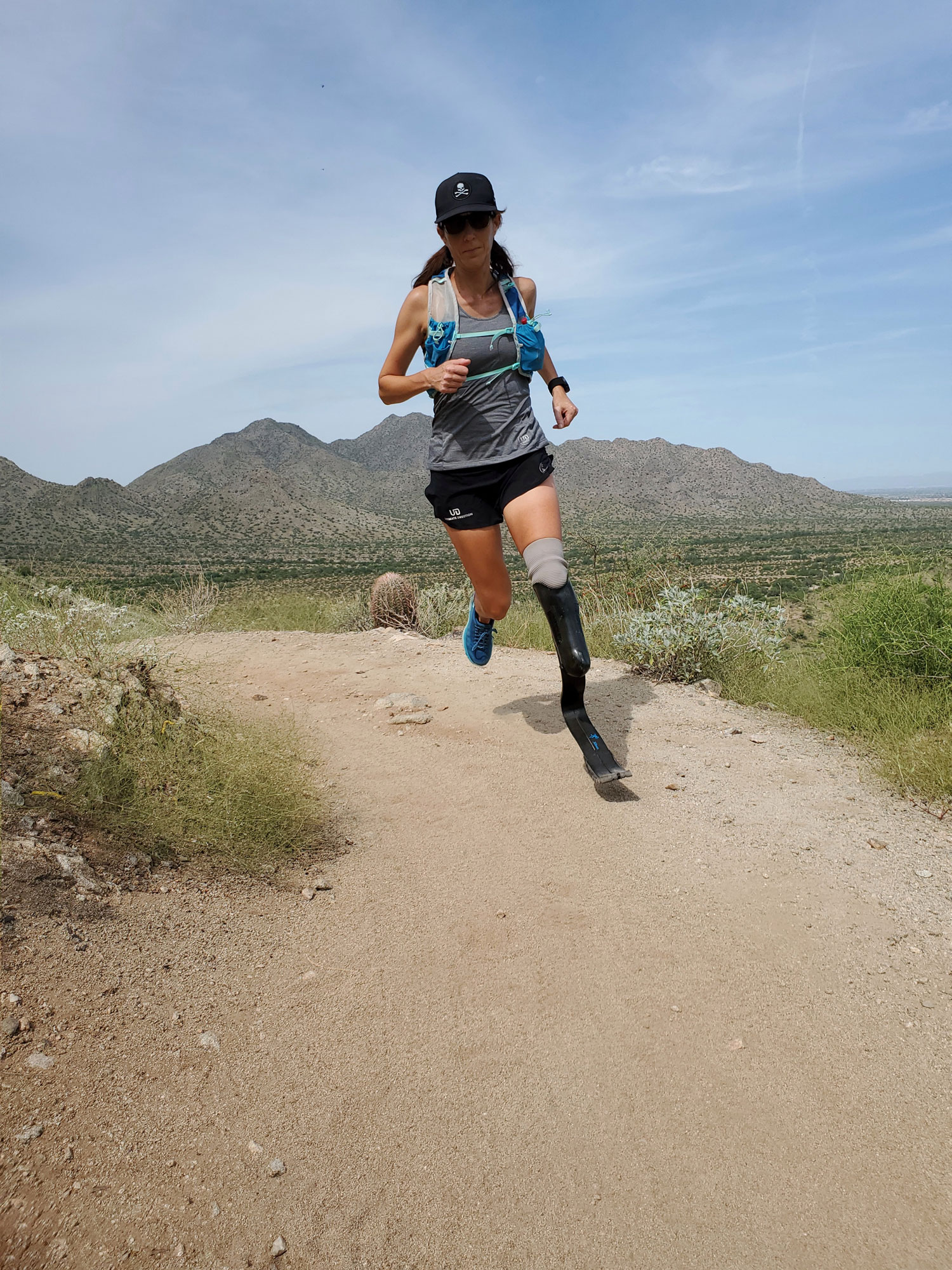 Amputee ultrarunner Jacky Hunt-Broersma runs on a dirt path with her running blade and brown mountains behind her.