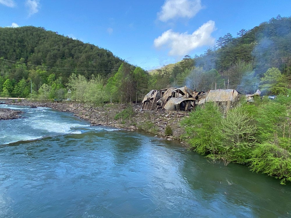 View of burned down Ocoee Whitewater Center from across the river during the day. Smoke still emits from the debris.
