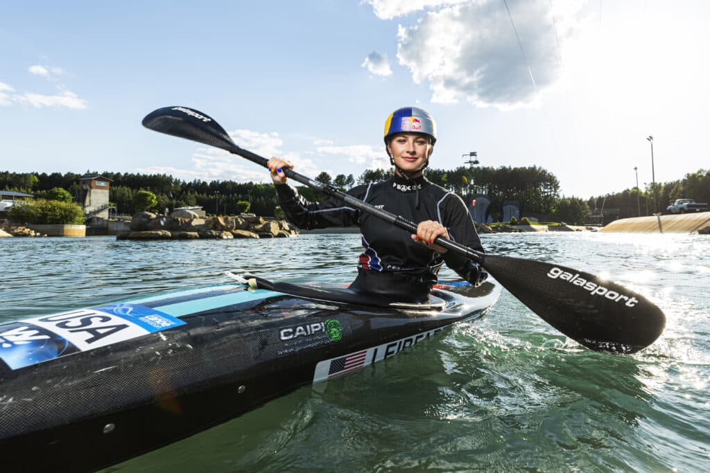Evy Leibfarth poses in a slamom kayak on the waters of the US National White Water Center while wearing a RedBull Helmet.