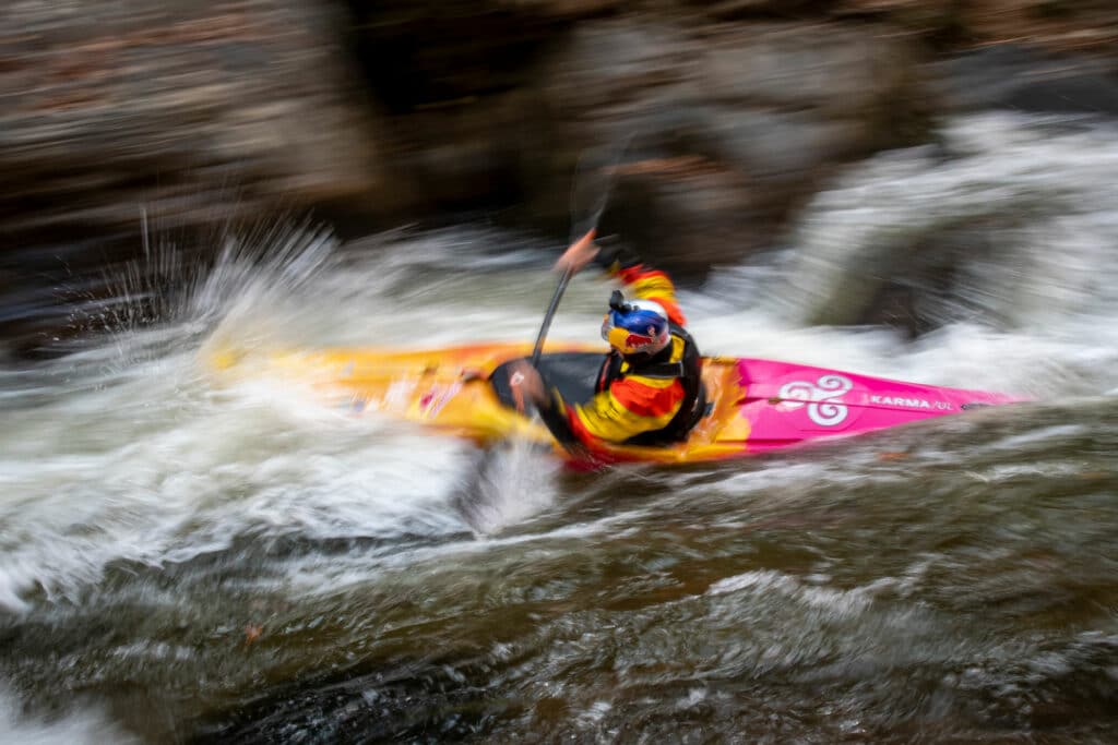 blurred photo of Dane Jackson moving quick through the Green River Narrows rapids during a training session. He is paddling a yellow and pink kayak for his training laps.