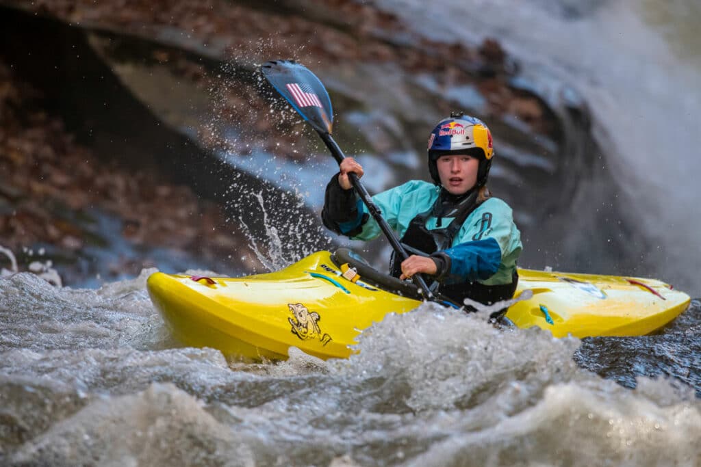 Evy Leibfarth paddles towards Gorilla rapid, the biggest drop on the Green River race course. She is wearing a Red Bull branded helmet and is paddling in a yellow whitewater kayak.