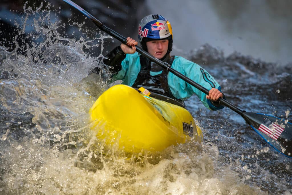 Evy Leibfarth paddling in big whitewater. She is wearing a Red Bull branded helmet and is paddling in a yellow whitewater kayak.