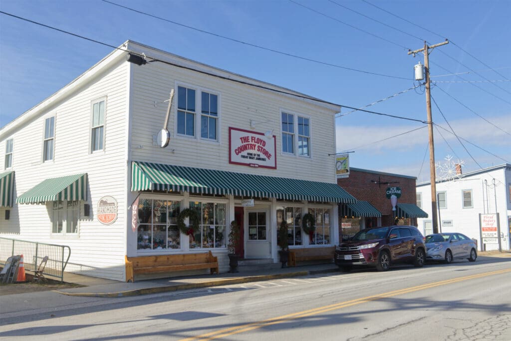 Photo of a white building with green awnings, big windows, and a sign in red writing that says "The Floyd Country Store"
