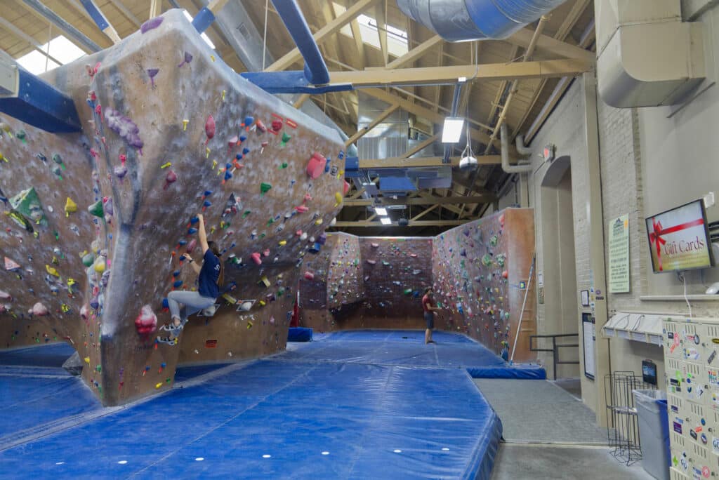 A climber scales a colorful rock wall in a indoor climbing gym.
