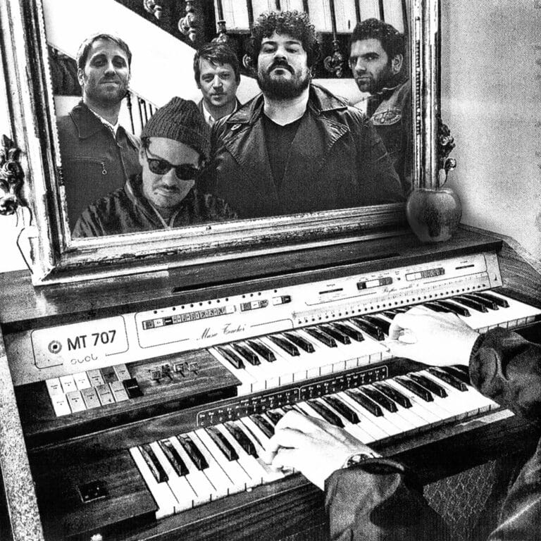 Black and white photo of 5 men's reflection in a mirrow while someone plays piano below it.