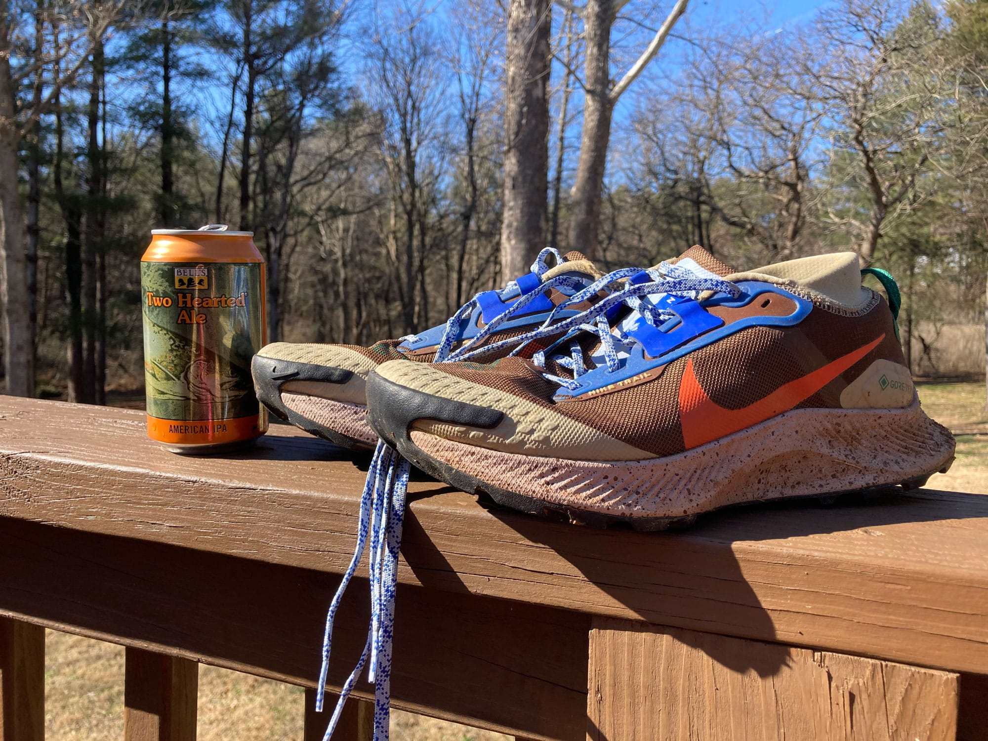 Running sneaker next to a can of beer on a wooden railing.