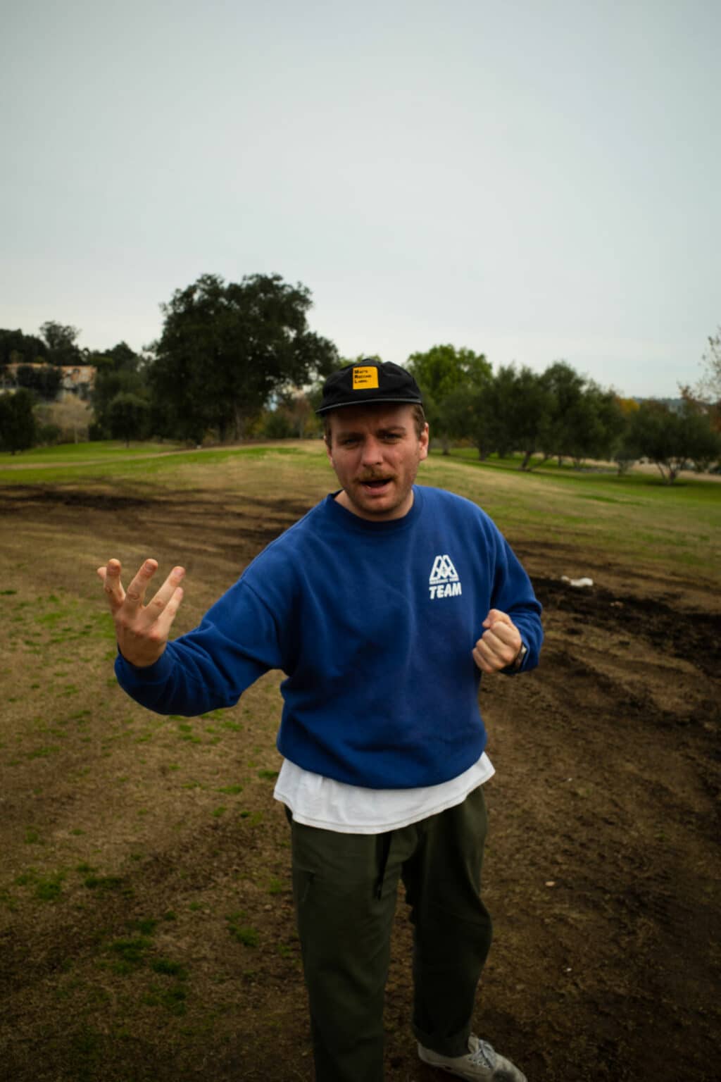 man sings in field with a black cap on and a blue sweatshirt.