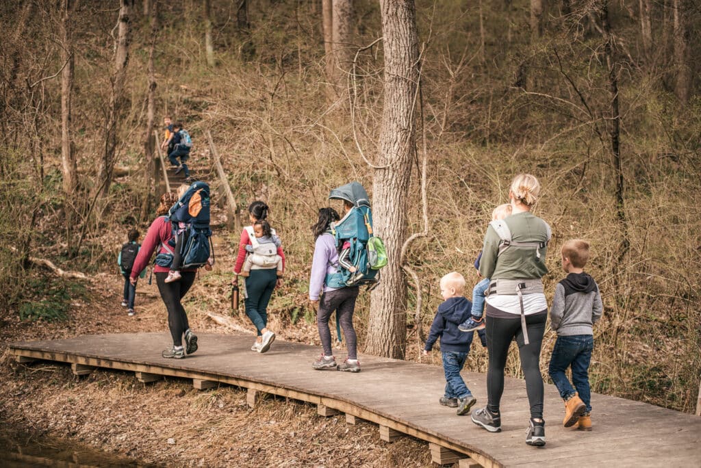 group of moms and kids walk across a wooden path in the woods