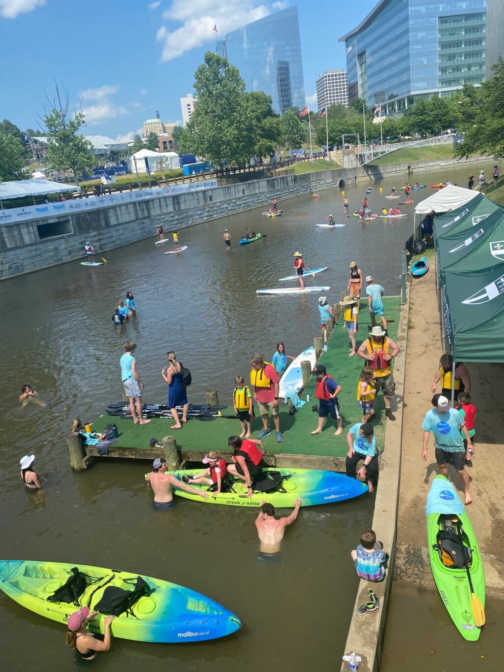 people gather near the edge of the water canal in downtown Richmond, Virginia to get in brightly colored kayaks.