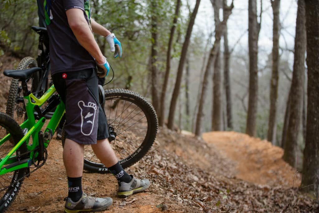 close up of a mountain bikers legs standing with a mountain bike on top of a dirt trail