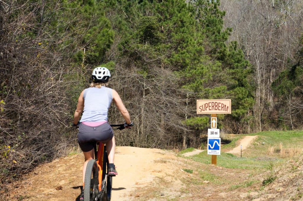 A mountain biker rides a undulating dirt path with a sign reading "Superberm"
